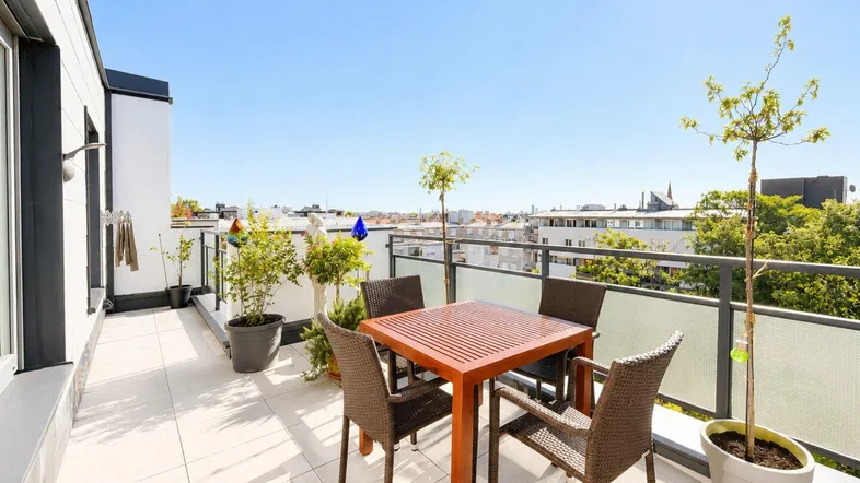 Sonnige Terrasse mit Esstisch und Stadtblick, ideal für Mahlzeiten im Freien.