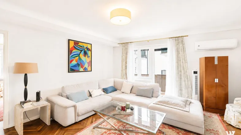 Helles Wohnzimmer mit bequemem Sofa, Parkettboden und Zugang zu einem Balkon, ausgestattet mit Klimaanlage.