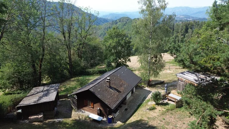 Luftaufnahme eines Hauses in ländlicher Umgebung mit bewaldeten Hügeln und Bergen.