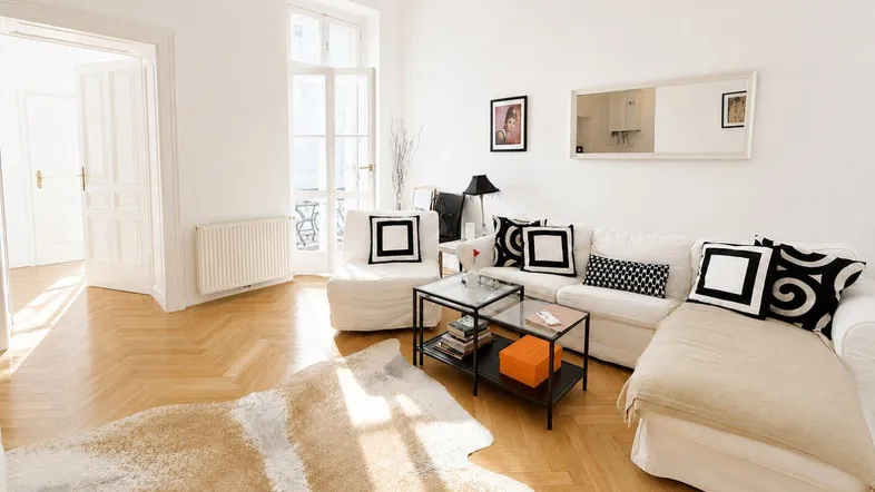 Helles Wohnzimmer mit elegantem Fischgrätparkett, hohen Decken und Zugang zu einem französischen Balkon.