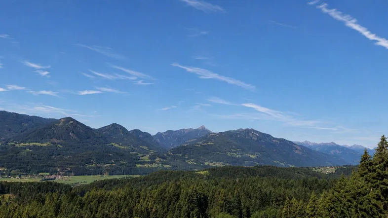 Weitläufiger Panoramablick auf die majestätischen Berge und die umliegende grüne Landschaft unter blauem Himmel.