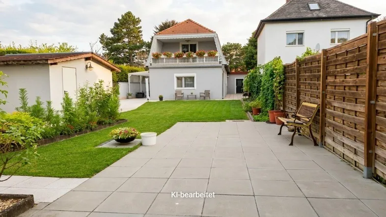 Gepflegter Gartenbereich mit Rasenfläche und gepflasterter Terrasse hinter dem Haus.