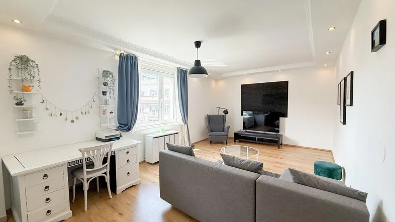 Helles Wohnzimmer mit Holzfußboden, gemütlichem Sofa, TV-Bereich und integriertem Arbeitsplatz.
