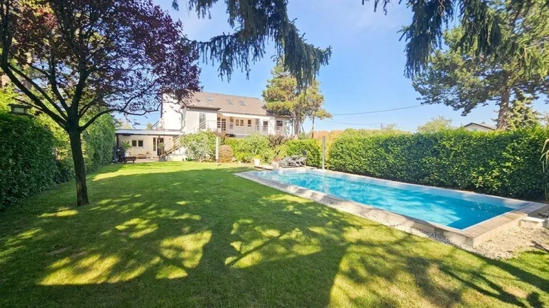 Großer Garten mit Rasenfläche und Swimmingpool, umgeben von Bäumen und Hecken.
