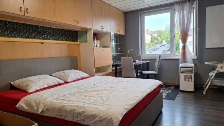Schlafzimmer mit integrierten Holzschränken, Bett und Blick auf die Straße.
