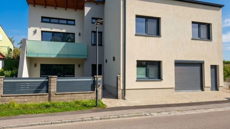 Moderne Fassade eines Einfamilienhauses mit Balkon und großen Fenstern.