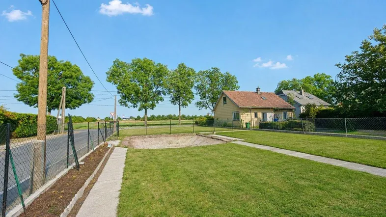 Gepflegter Vorgarten mit Rasenfläche und Gehweg, umgeben von ländlicher Natur und einem Einfamilienhaus im Hintergrund.