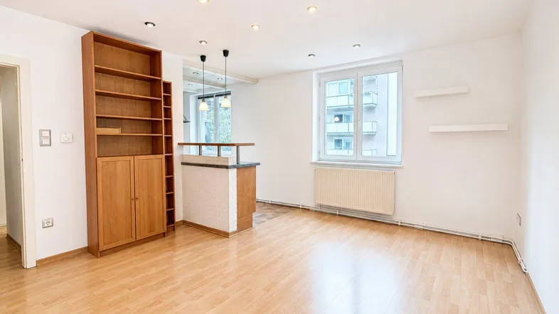 Helles Wohnzimmer mit Holzboden, Einbauregal und einer Theke zum Küchenbereich.