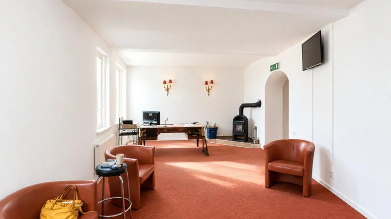 Geräumiges Büro oder Empfangsbereich mit Teppichboden, Kaminofen und hohen Decken.