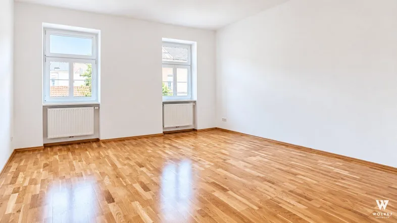 Helles Zimmer mit Parkettboden und zwei Fenstern, ideal als Wohn- oder Schlafzimmer.
