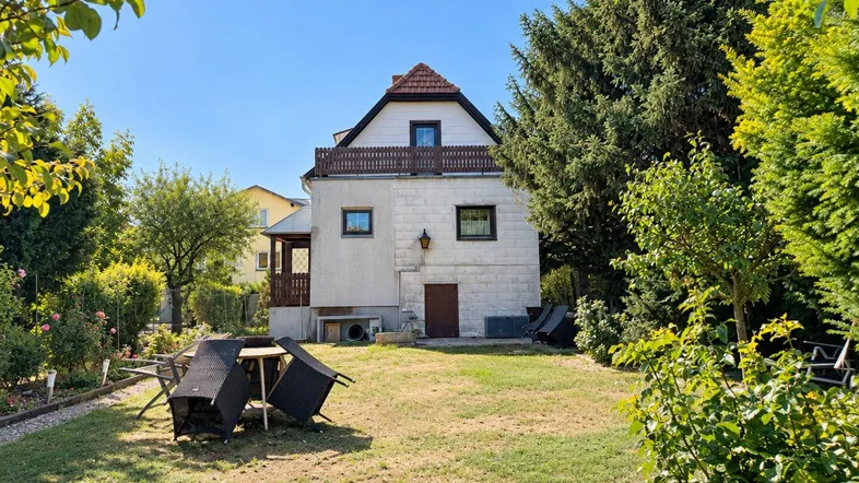 Großzügiger Gartenbereich mit Rasenfläche und Sitzgelegenheiten hinter dem Haus unter blauem Himmel.