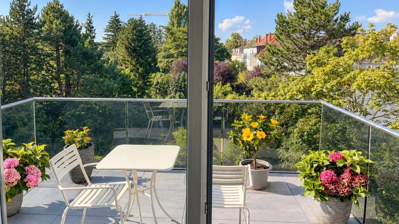 Moderner Balkon mit Glasgeländer, Sitzgelegenheiten und weitem Blick ins Grüne.