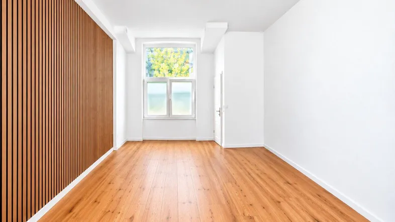 Heller, leerer Raum mit Holzboden, weiß gestrichenen Wänden und einer dekorativen Lamellenwand.