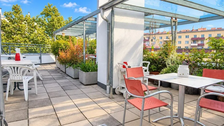 Geräumige Dachterrasse mit Sitzgelegenheiten, Pflanzen und Glasüberdachung, ideal zum Entspannen.