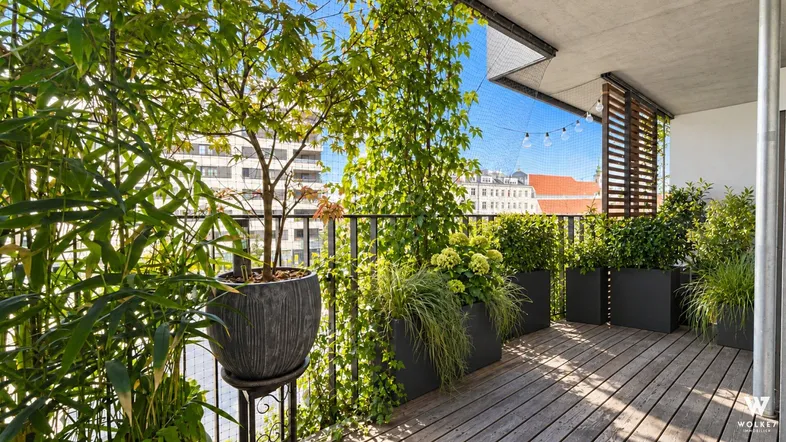 Heller Balkon mit Holzboden, üppiger Bepflanzung und Blick auf die Stadt.