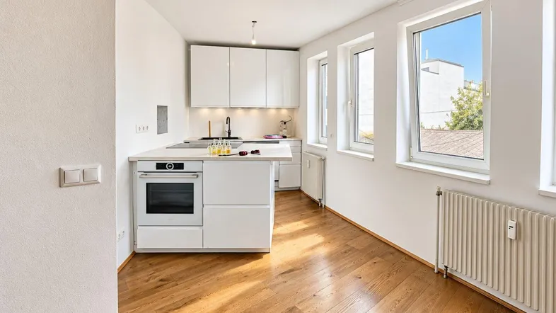 Moderne, helle Küche mit weißen Hochglanzschränken, integriertem Backofen und Holzboden.
