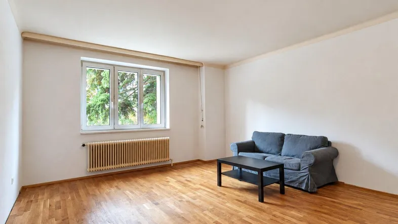 Helles Wohnzimmer mit Parkettboden, weiß gestrichenen Wänden und Blick ins Grüne.