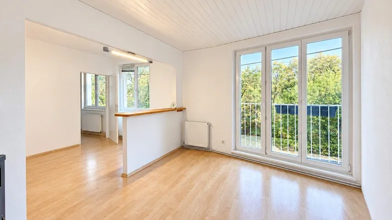 Helles Wohnzimmer mit Parkettboden, weißen Wänden und Zugang zu einem Balkon mit Blick ins Grüne.