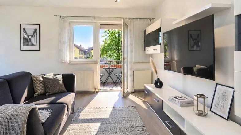 Helles Wohnzimmer mit modernem Medienmöbel, Sofa und Zugang zu einem kleinen Balkon.