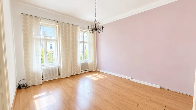 Helles Zimmer mit rosa Wänden, Laminatboden und zwei großen Fenstern, die viel Tageslicht hereinlassen.