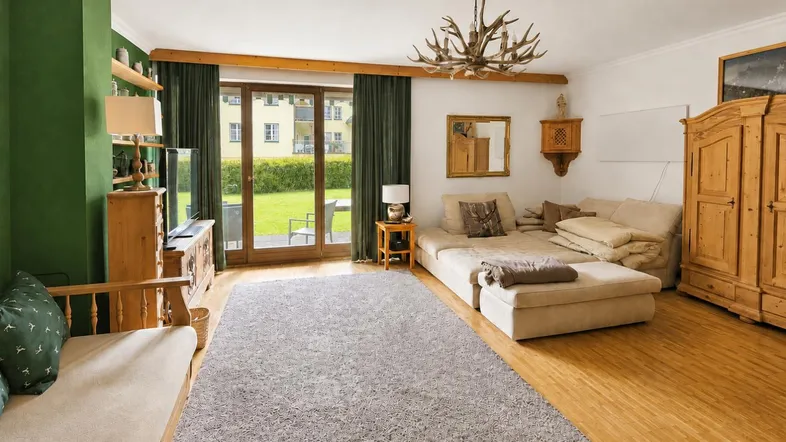 Gemütliches Wohnzimmer im alpinen Stil mit Holzboden, grüner Akzentwand und Zugang zum Garten.