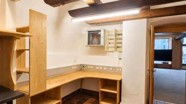 Funktionaler Büroraum mit sichtbaren Holzbalken, eingebautem Schreibtisch und Terrakotta-Fliesenboden.