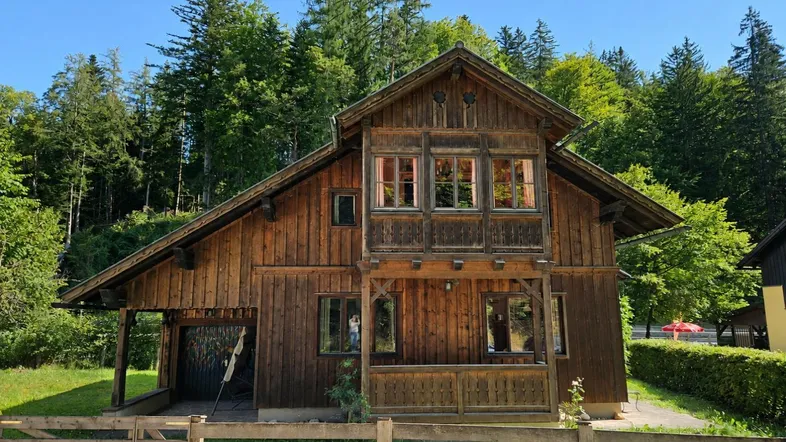 Traditionelles Holzhaus im Chalet-Stil, umgeben von grüner Natur und Bäumen.
