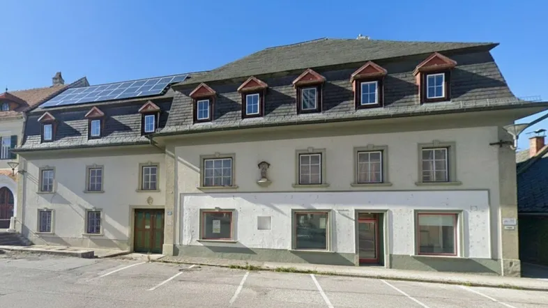 Altes Gebäude mit Mansarddach und Solarpaneelen auf dem Dach, umgeben von Parkplätzen.