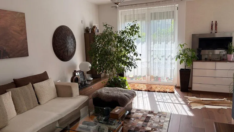 Gemütliches Wohnzimmer mit hellem Sofa, Holzboden und Zugang zu einem Balkon oder einer Terrasse.