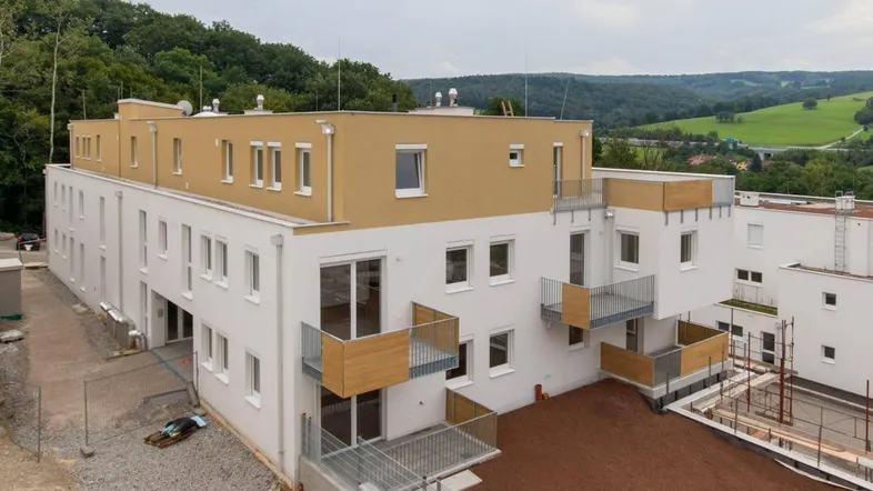 Modernes Mehrfamilienhaus mit Balkonen und Terrassen in ländlicher Umgebung, umgeben von viel Grün.