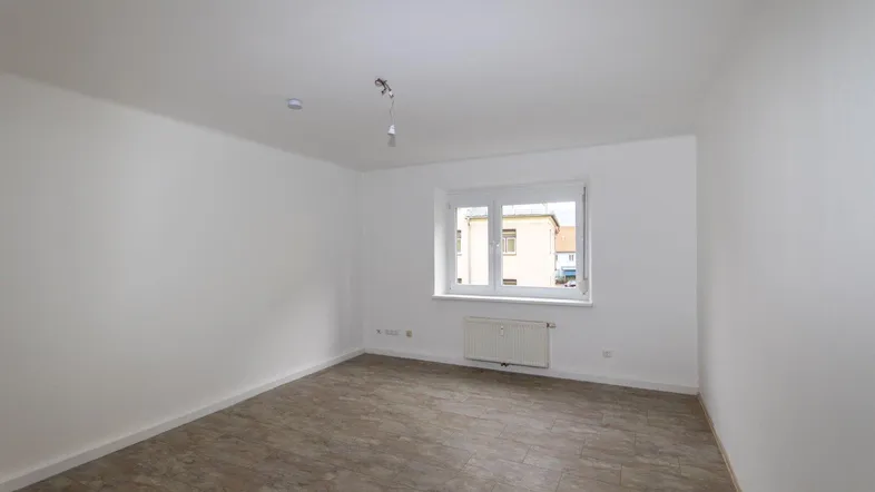 Helles, leeres Zimmer mit Laminatboden und Fenster, bereit zur individuellen Gestaltung.