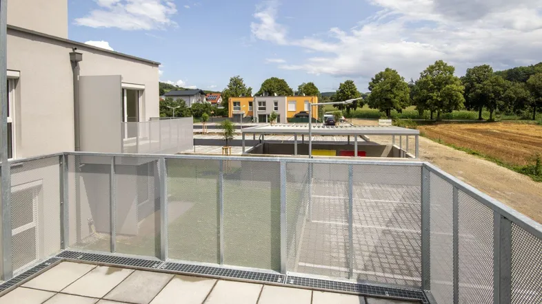 Geräumige Terrasse mit Fliesenboden und Blick auf die Umgebung sowie den Parkplatz.