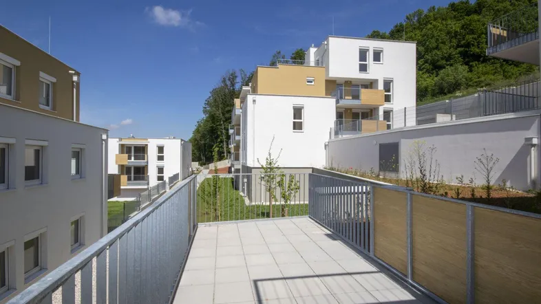 Geräumige Terrasse mit Fliesenboden und Blick auf die umliegenden Neubauten und grüne Hügel.