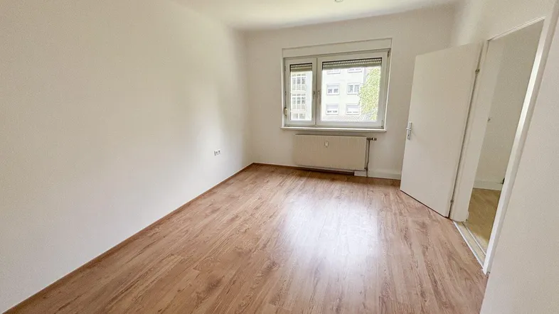 Leerer Raum mit Laminatboden und Fenster, bereit zur individuellen Gestaltung.