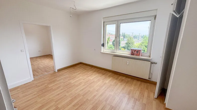 Helles Zimmer mit Laminatboden und Fensterblick ins Grüne, bereit zur individuellen Gestaltung.