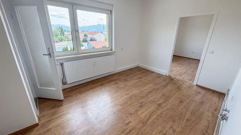 Helles Zimmer mit Laminatboden und Fensterblick auf die Umgebung und Berge.