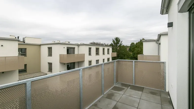 Geräumiger Balkon mit Fliesenboden und moderner Metallbrüstung, mit Blick auf Neubauten.