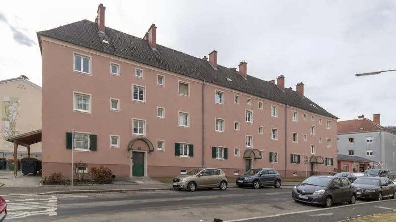 Mehrfamilienhaus mit rosafarbener Fassade und Satteldach, von der Straße aus gesehen.