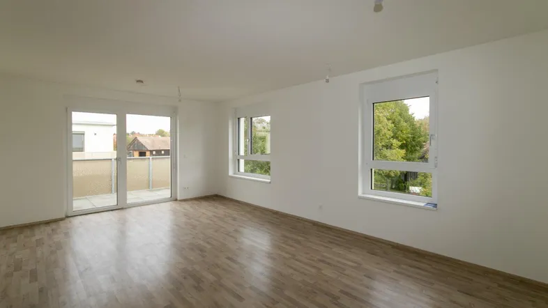 Helles, leeres Zimmer mit Laminatboden und Zugang zu einem Balkon, ideal für Wohn- oder Schlafbereich.