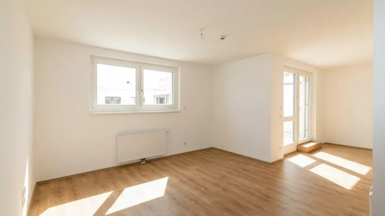 Helles, leeres Zimmer mit Laminatboden und Zugang zu einem Balkon, ideal für Wohn- oder Schlafbereich.