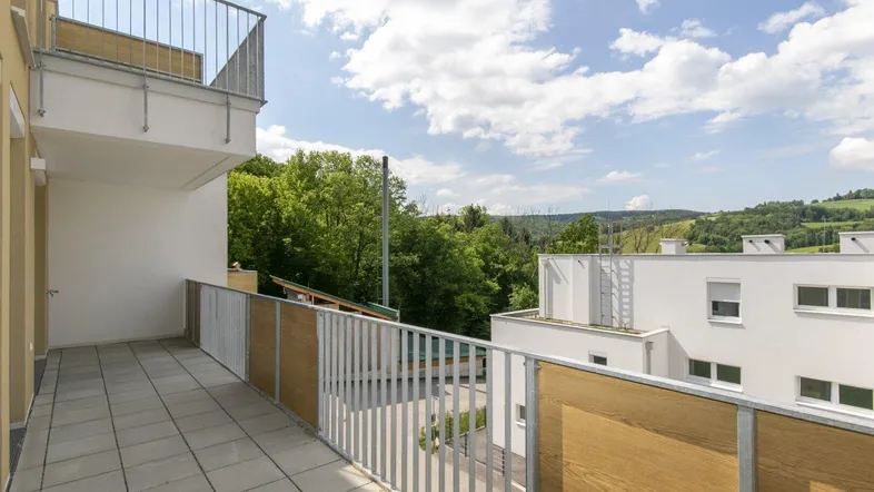 Geräumiger Balkon mit Fliesenboden und Blick auf die grüne Hügellandschaft und umliegende Gebäude.