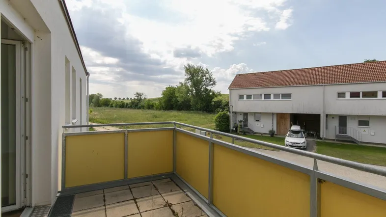 Geräumiger Balkon mit Blick auf grüne Felder und die umliegende Wohnsiedlung.