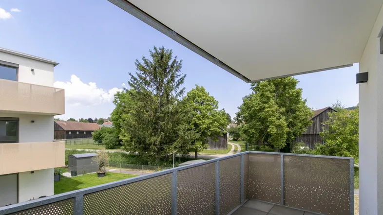 Moderner Balkon mit Fliesenboden und Blick ins Grüne sowie auf umliegende Gebäude.