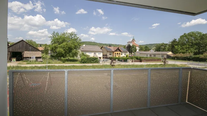 Balkon mit Fliesenboden und weitem Blick über die ländliche Umgebung und eine Kirche.