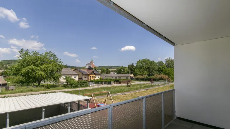 Heller Balkon mit Blick auf die ländliche Umgebung, einen Spielplatz und einen Kirchturm.