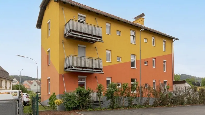 Gebäude mit auffälliger gelb-oranger Fassade und zwei Balkonen unter blauem Himmel.