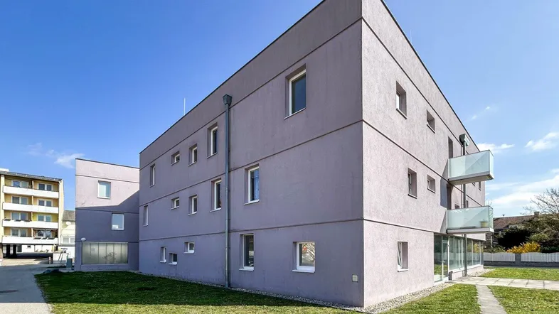 Modernes Mehrfamilienhaus mit schlichter Fassade und kleinen Balkonen unter blauem Himmel.