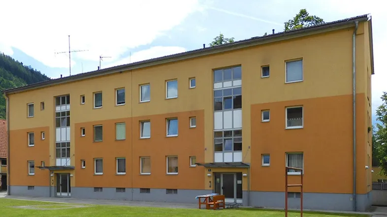 Mehrfamilienhaus mit gelb-orangefarbener Fassade und gepflegter Grünfläche im Vordergrund.
