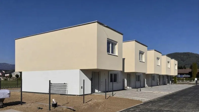 Reihe moderner Neubauten mit flachen Dächern und heller Fassade unter blauem Himmel.