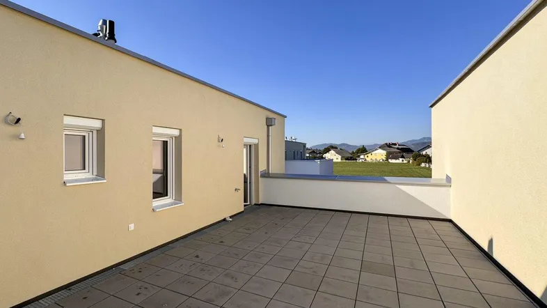 Geräumige Dachterrasse mit Fliesenboden und weitem Blick auf die umliegende Landschaft und Berge.